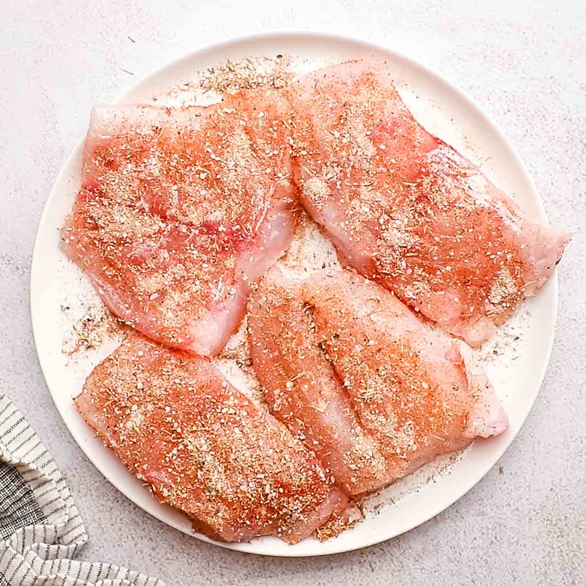 A plate with 4 fish filets coated with Cajun seasoning.