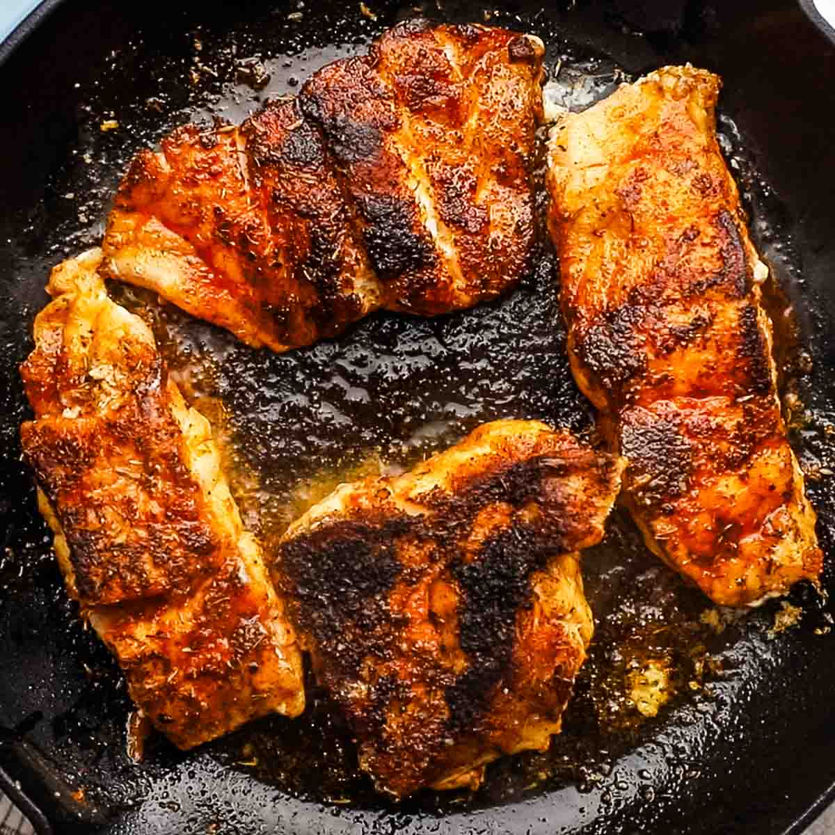 4 blackened fish filets in a cast iron skillet.