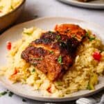 A side view of a filet of blackened fish on a bed of rice pilaf.