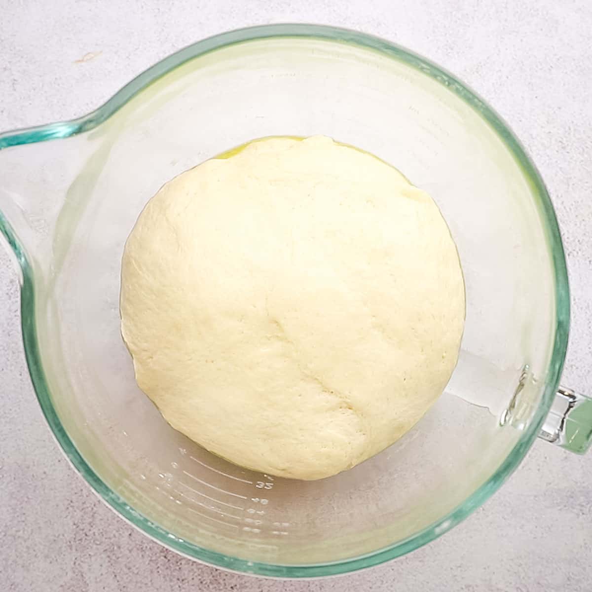 A risen ball of pizza dough in a mixing bowl.