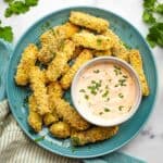 Overhead view of a plate of breaded halloumi fries on a blue plate with a bowl of harissa yogurt dip