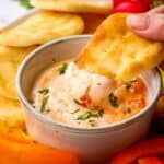 A mini pita bread being dipped into a bowl of harissa yogurt dip.
