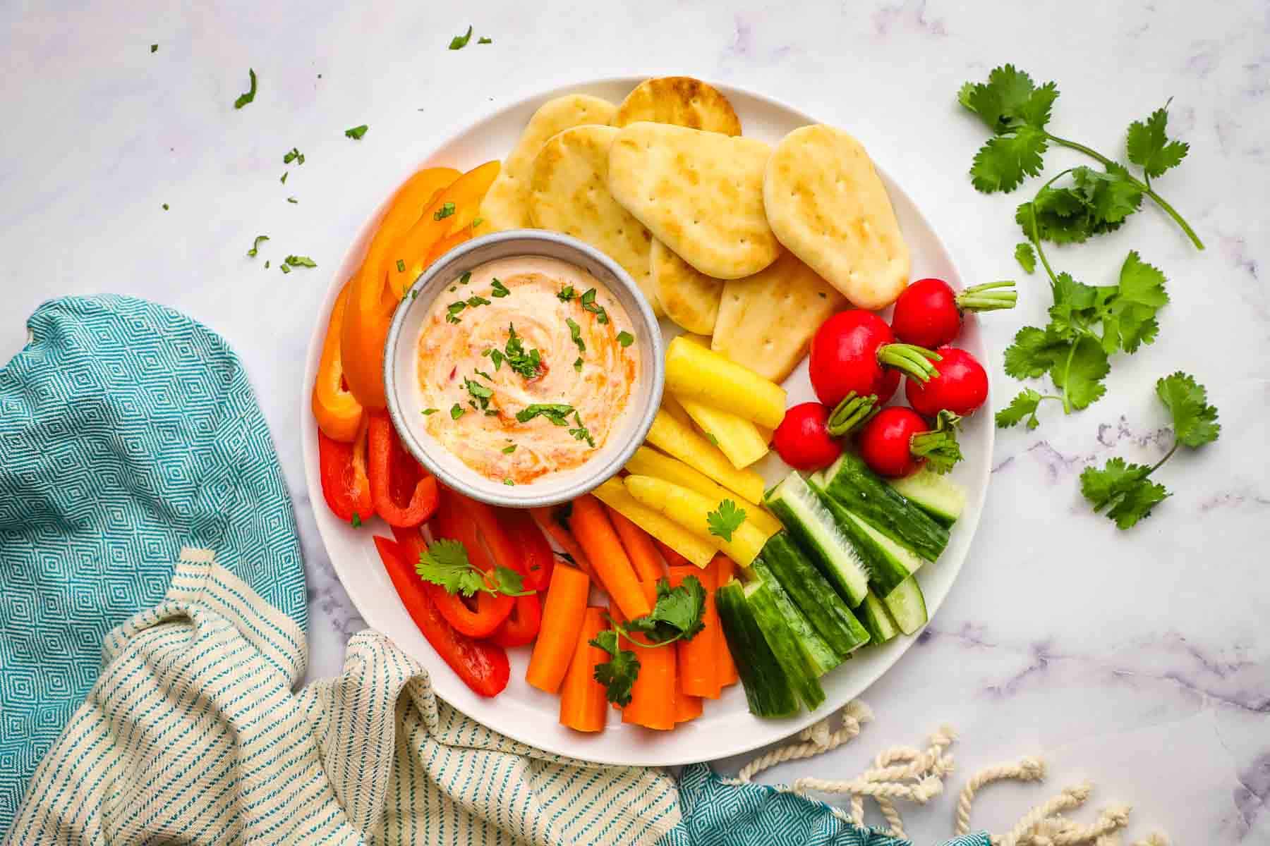 an overhead view of a vegetable and pita bread platter with harissa yogurt dip in the middle