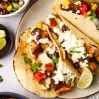 A plate of blackened fish tacos garnished with corn and black bean salsa, crema, queso fresco and cilantro.