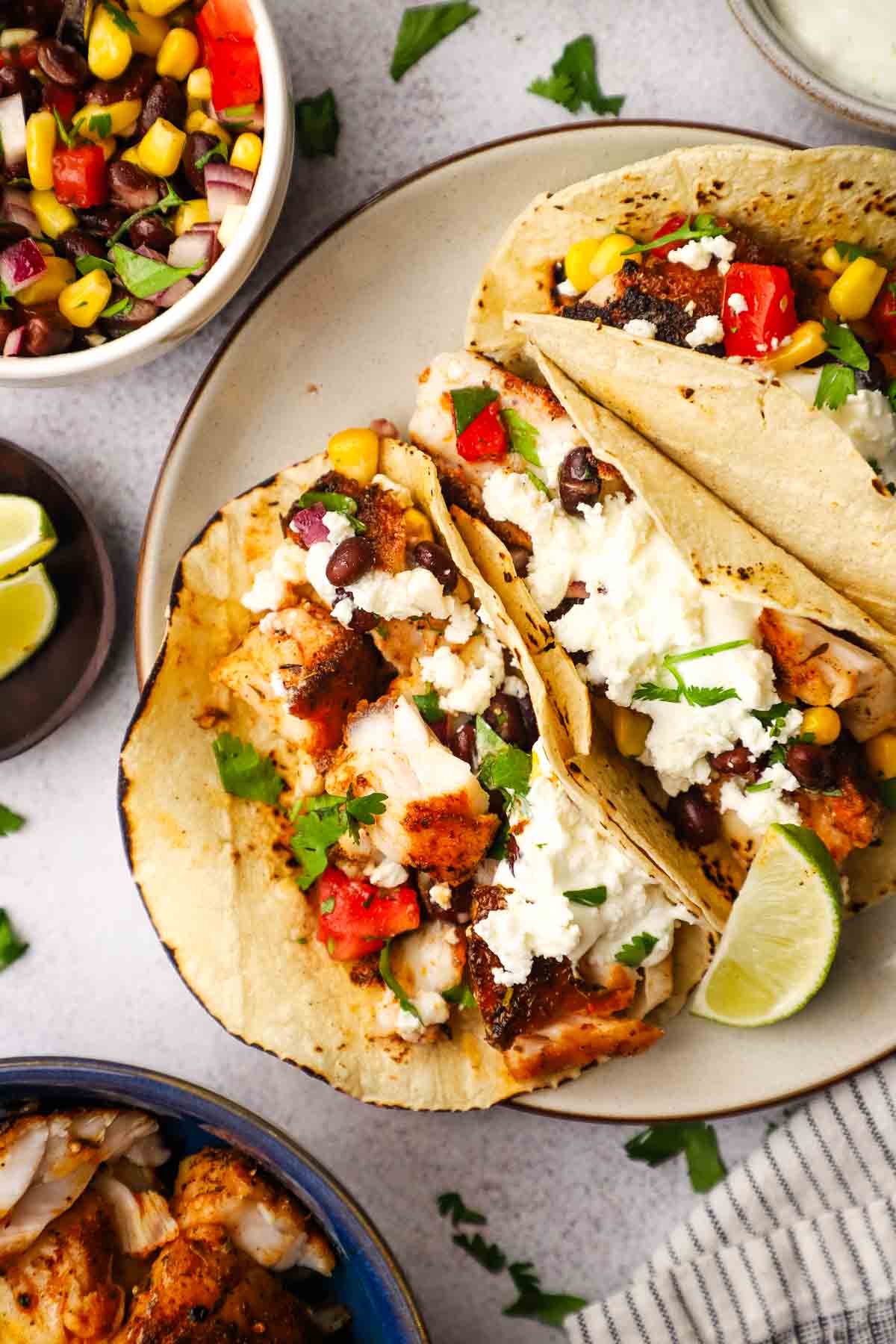 A plate of blackened fish tacos garnished with corn and black bean salsa, crema, queso fresco and cilantro.