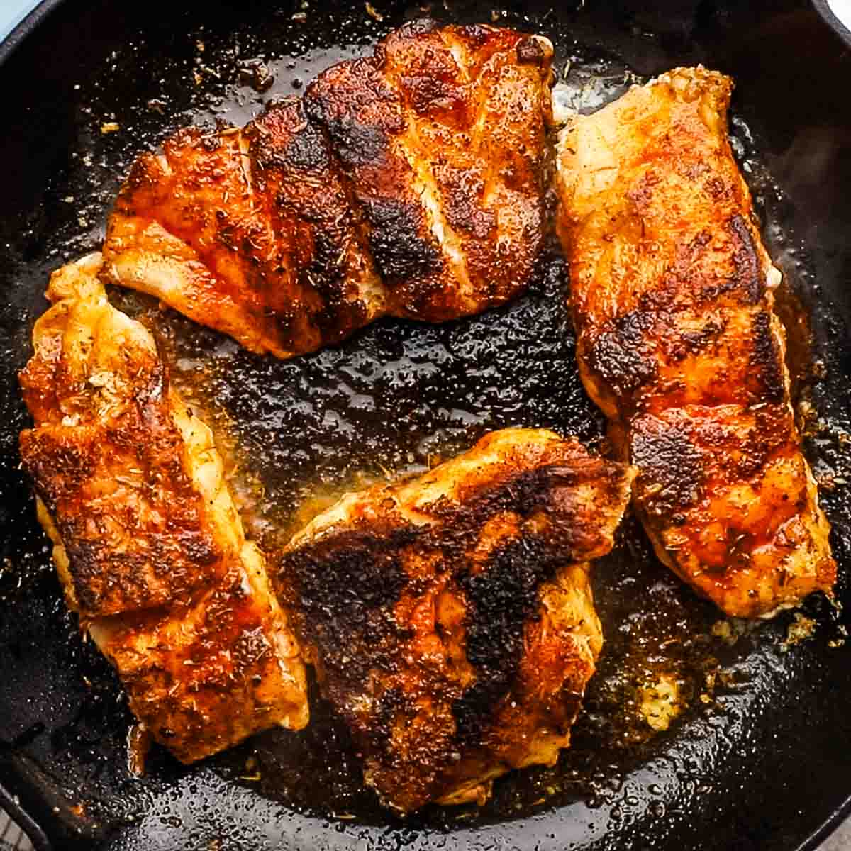 4 blackened fish pieces in a cast iron pan.
