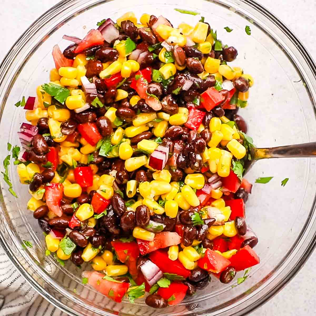 Corn and black bean salsa in a bowl with serving utensils.
