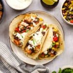 Overhead view of 3 tacos with bowls of toppings surrounding it.
