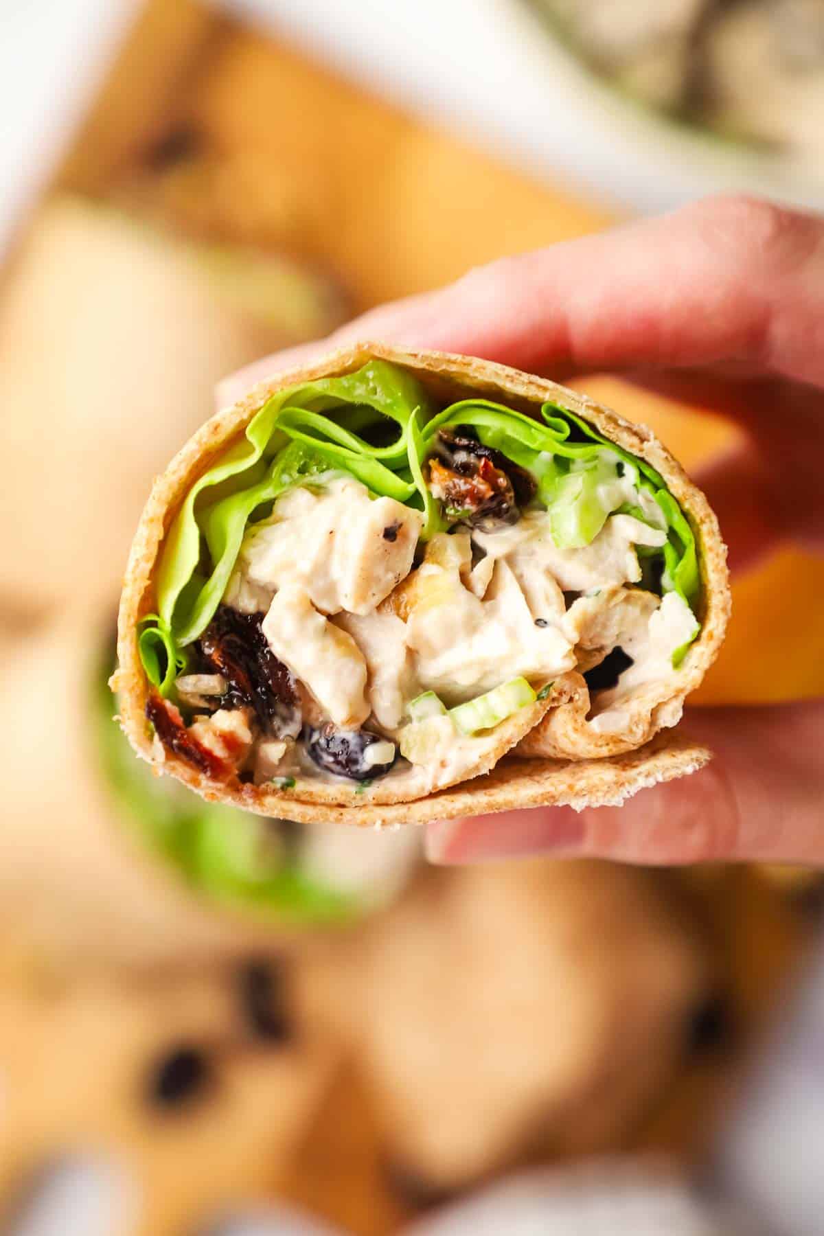 Hand holding up half a chicken salad wrap to show a closeup of the inside.