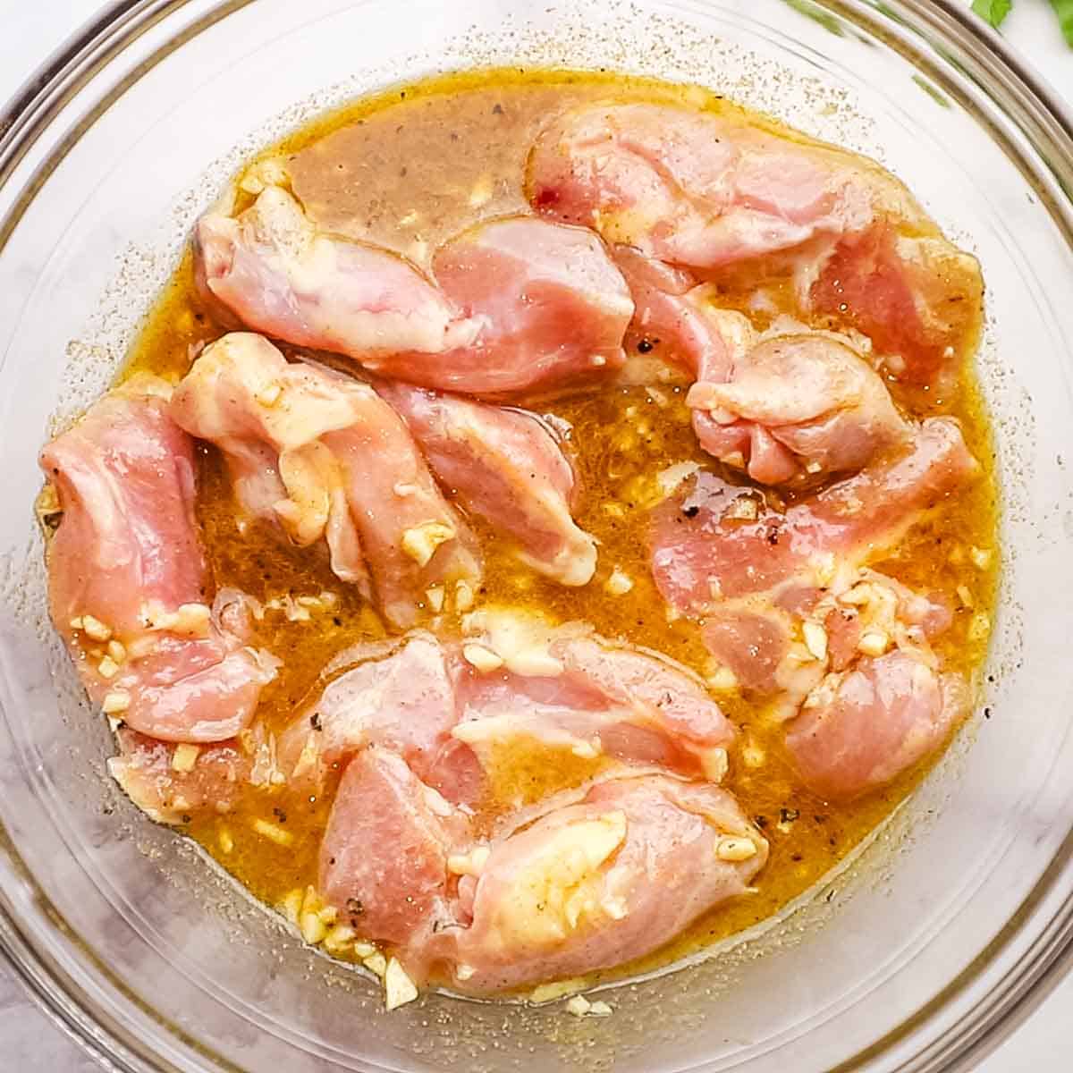 chicken being marinated in a big bowl