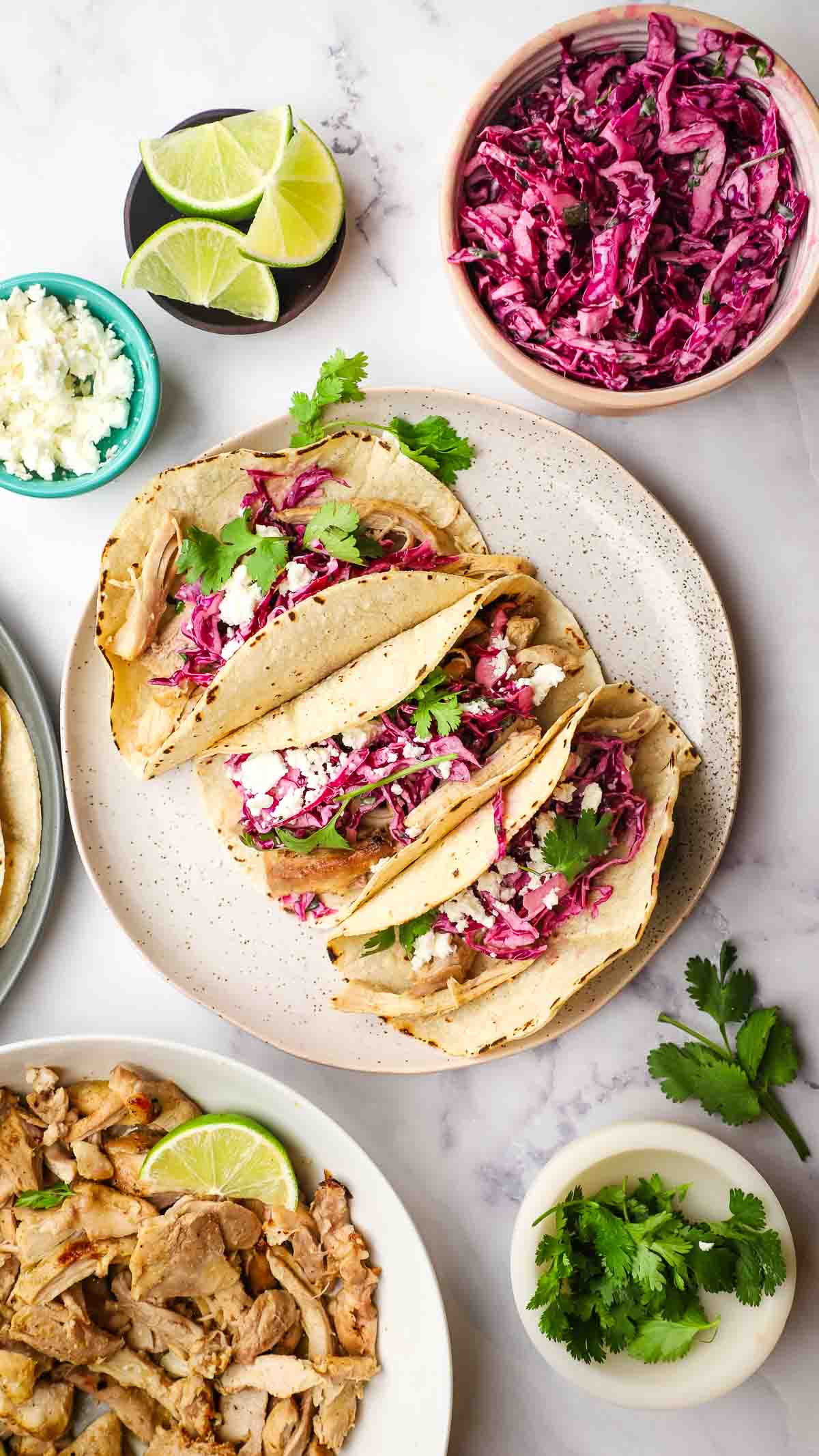 three chicken tacos with cilantro lime slaw in a plate with the toppings and ingredients in the background