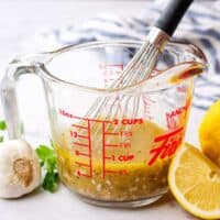 A greek marinade in a measuring cup with a whisk in it.