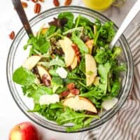 Overhead view of a bowl of mixed apple pecan salad with serving utensils in it.