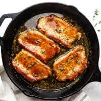 4 boneless cooked pork chops in a cast iron pan, with a maple glaze and garnished with fresh thyme.