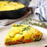 Side view of a slice of sweet potato fritatta on a plate with the pan in the background.