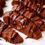 Closeup of chocolate almons biscotti drizzled with chocolate on a parchment lined baking sheet.