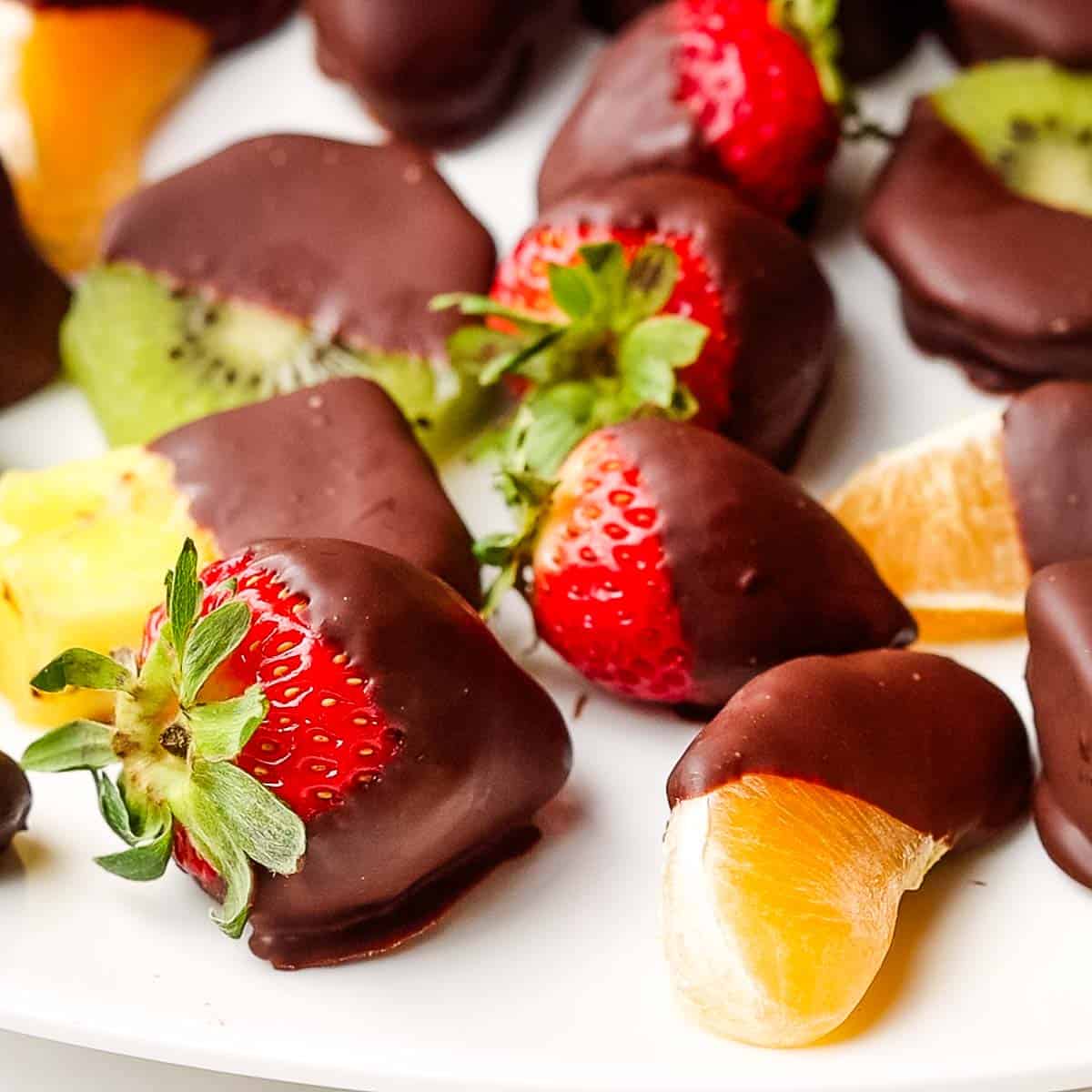 Various fruits dipped in chocolate on a white platter.