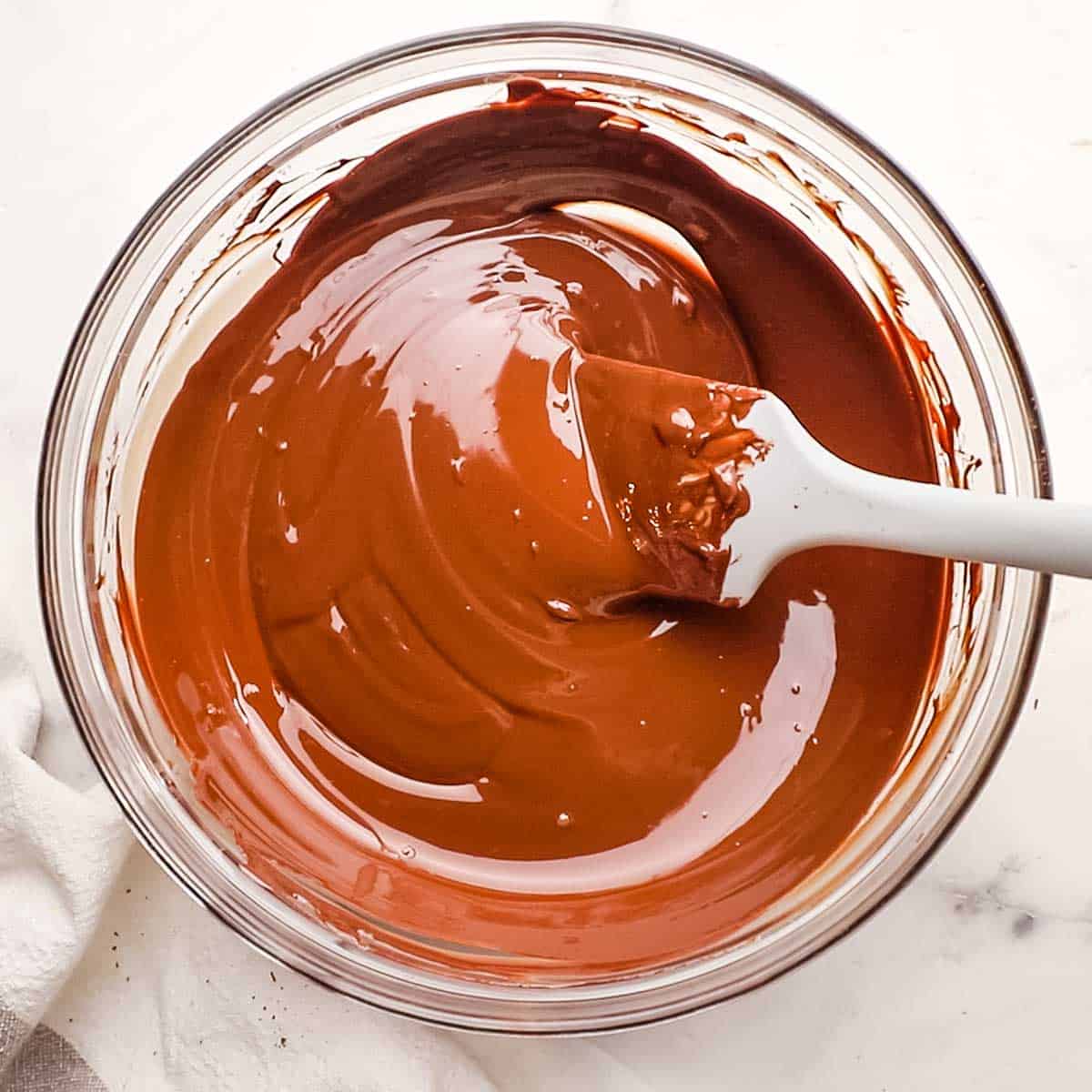 A bowl of tempered chocolate with a gray silicone spatula in it.