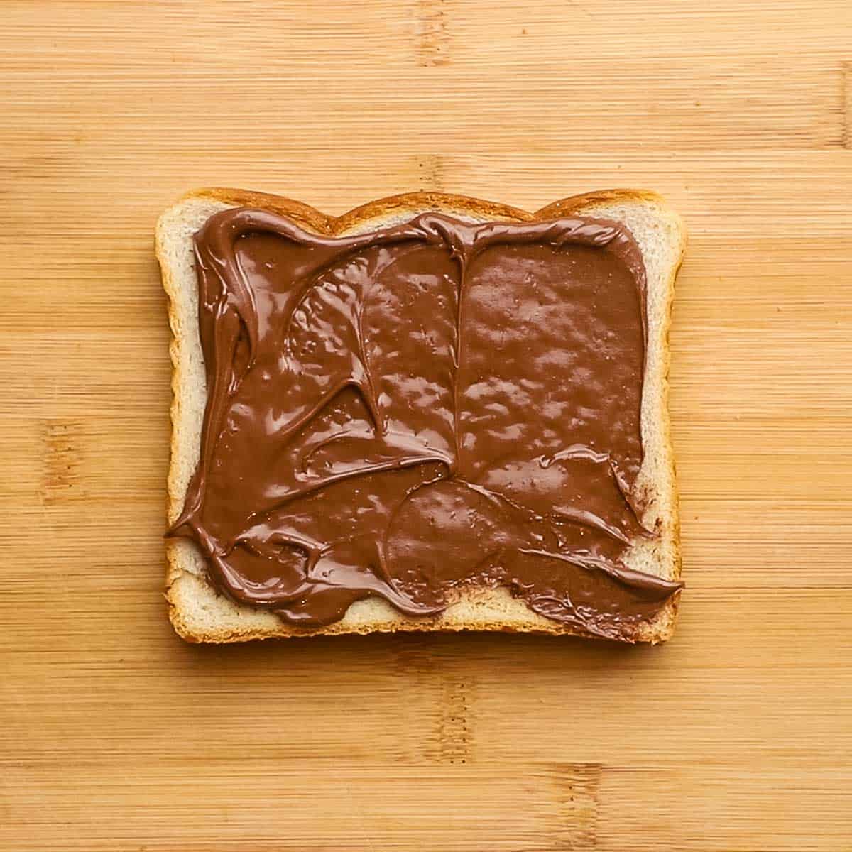 nutella spread on a slice of bread placed on a cutting board