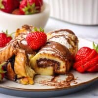 A plate of rolled nutella French toast garnished with fresh strawberries, with one roll sliced open to show the inside.