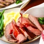 Gravy being poured over a plate of roast beef.