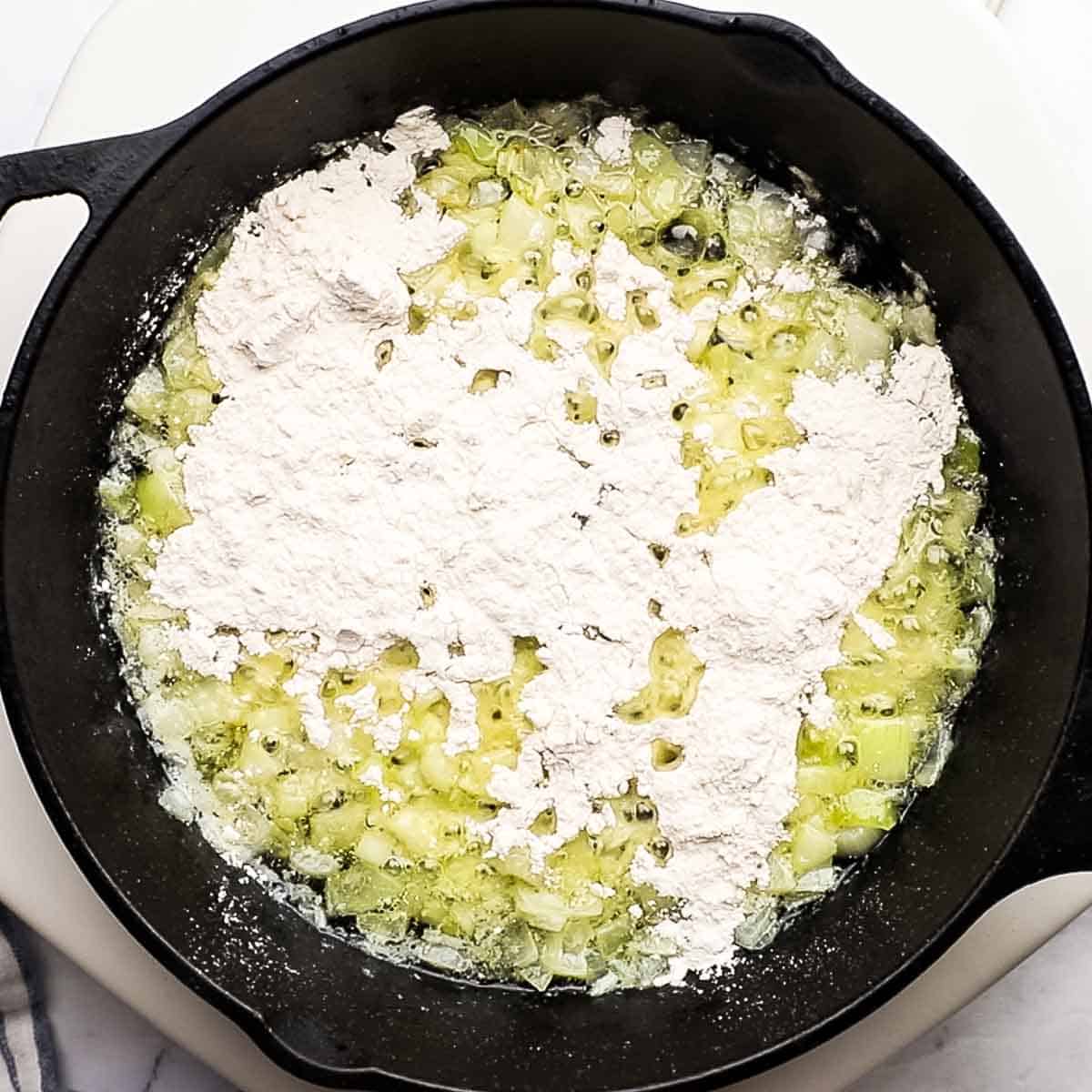 all-purpose flour added to a skillet with softened onions