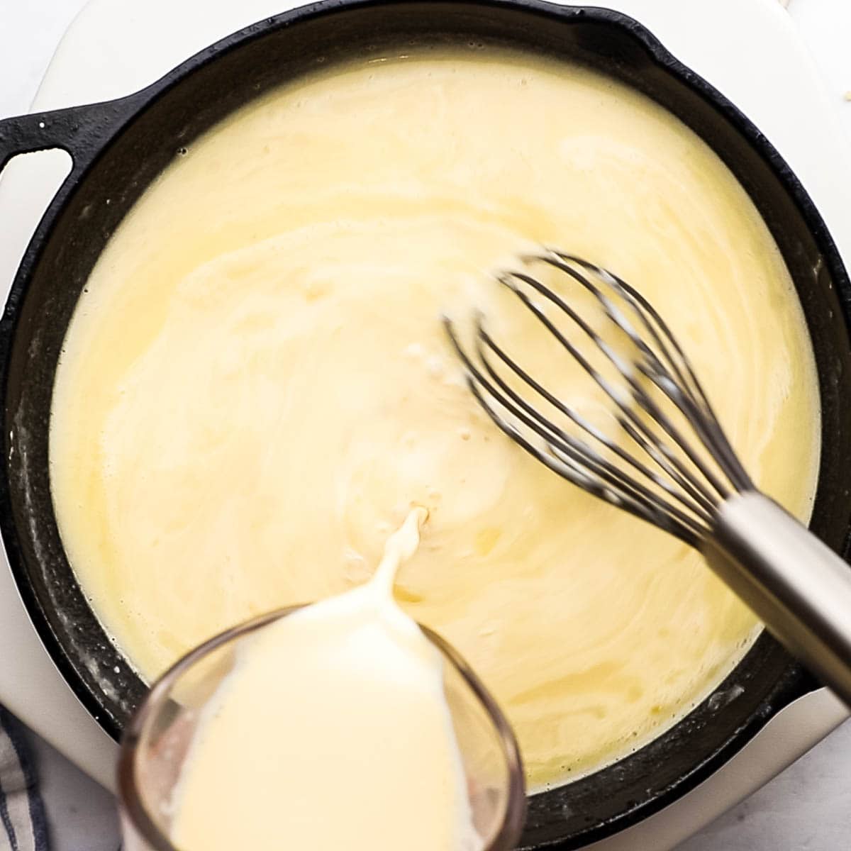 adding evaporated milk to the skillet while whisking