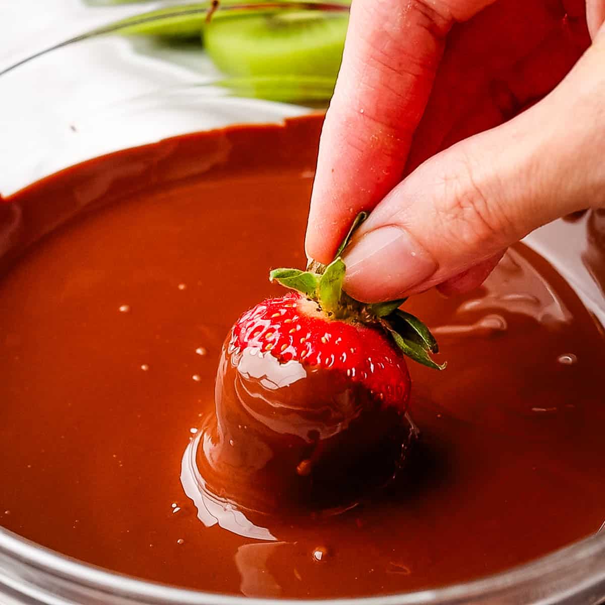 A strawberry being dipped in a bowl of melted chocolate.