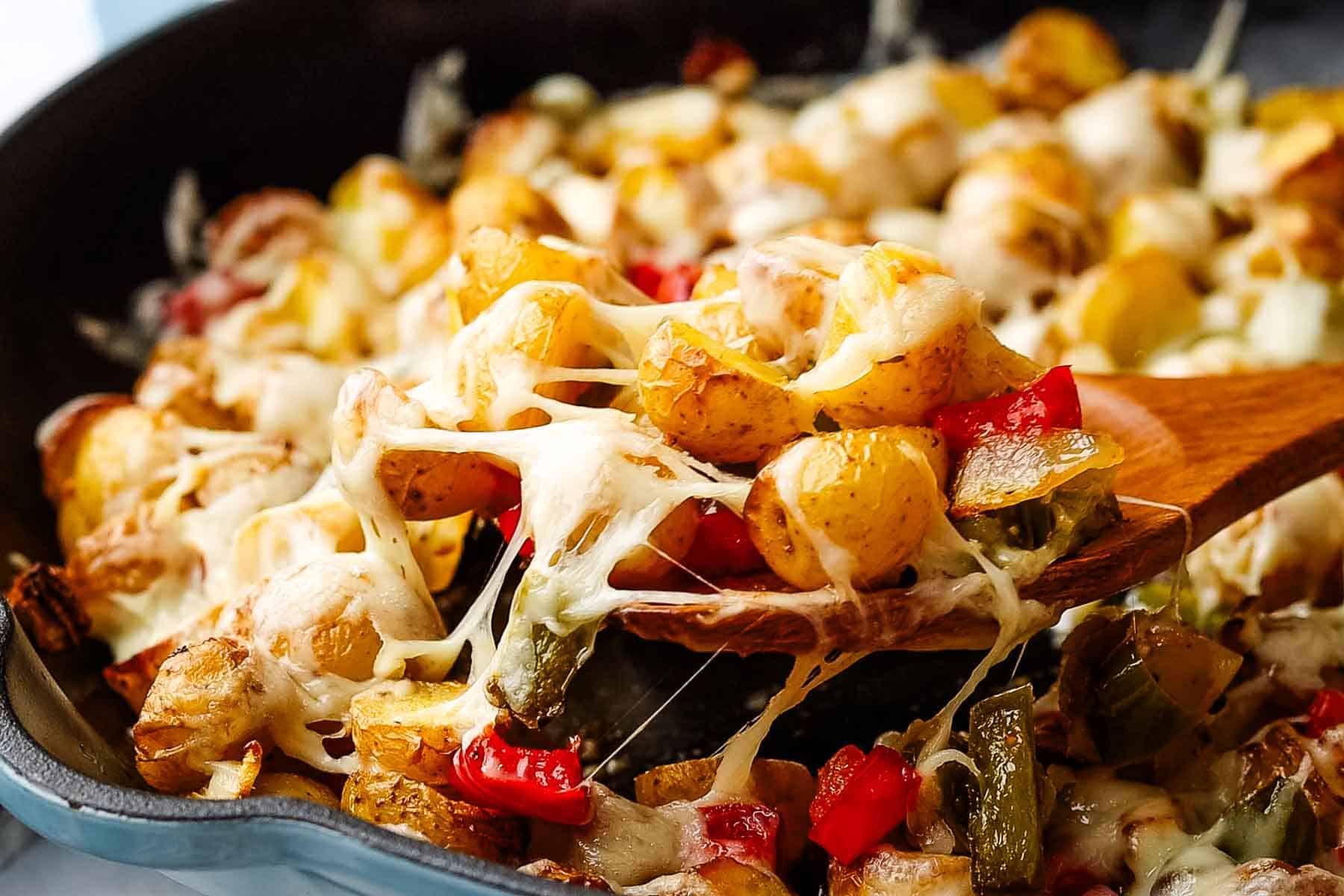 cheesy country potatoes in a skillet with a wooden spoon in it