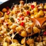 A cast iron pan of roasted breakfast potatoes and peppers with a wooden spatula lifting some out.