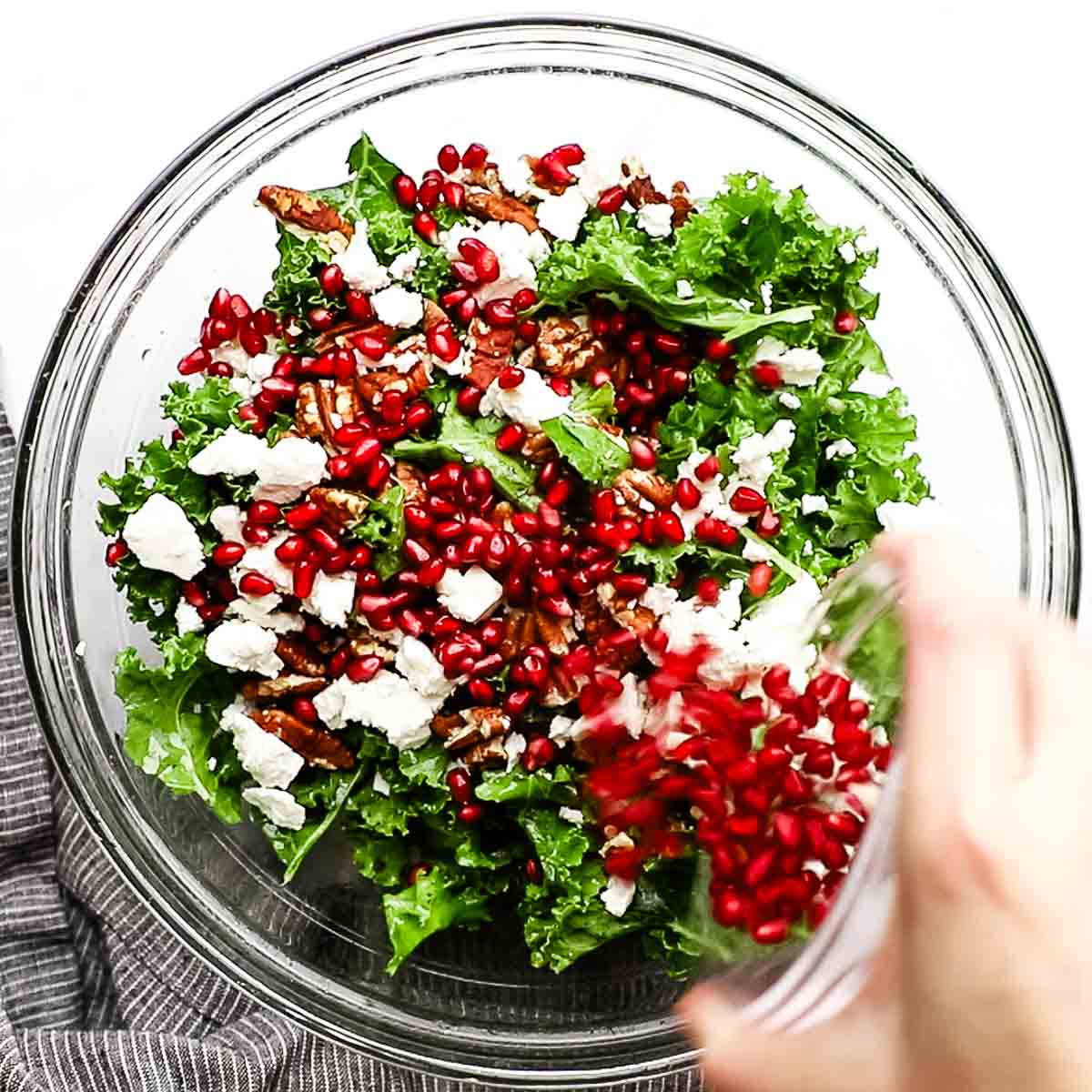 topping kale leaves combined with feta cheese and toasted pecans with pomegranate seeds