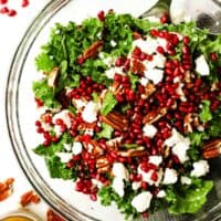 Overhead view of a bowl of kale salad topped with pomegranate arils and feta cheese and pecans.