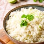 Side closeup view of a serving bowl of white rice garnished with a sprig of cilantro.
