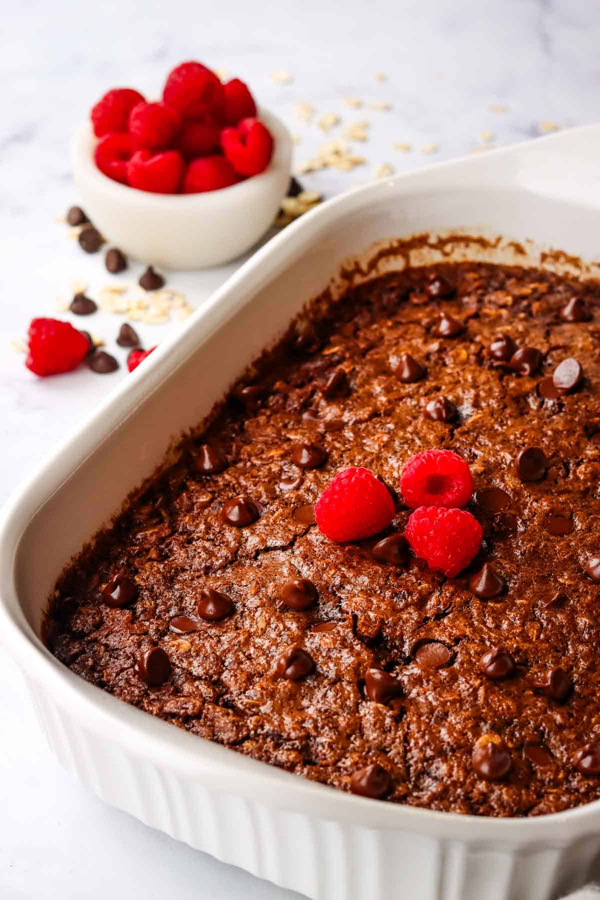 chocolate baked oats in a baking dish topped with fresh raspberries