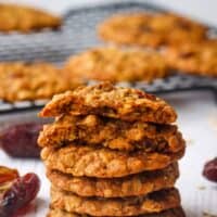 A stack of oatmeal date cookies with the one on top broken in half to show the inside.