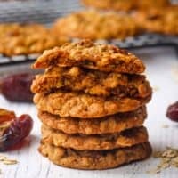 A stack of oatmeal date cookies with the one on top broken in half to show the inside.