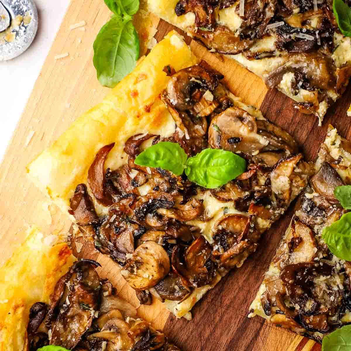 Overhead closeup of a piece of mushroom tart garnished with fresh basil on a wooden cutting board.