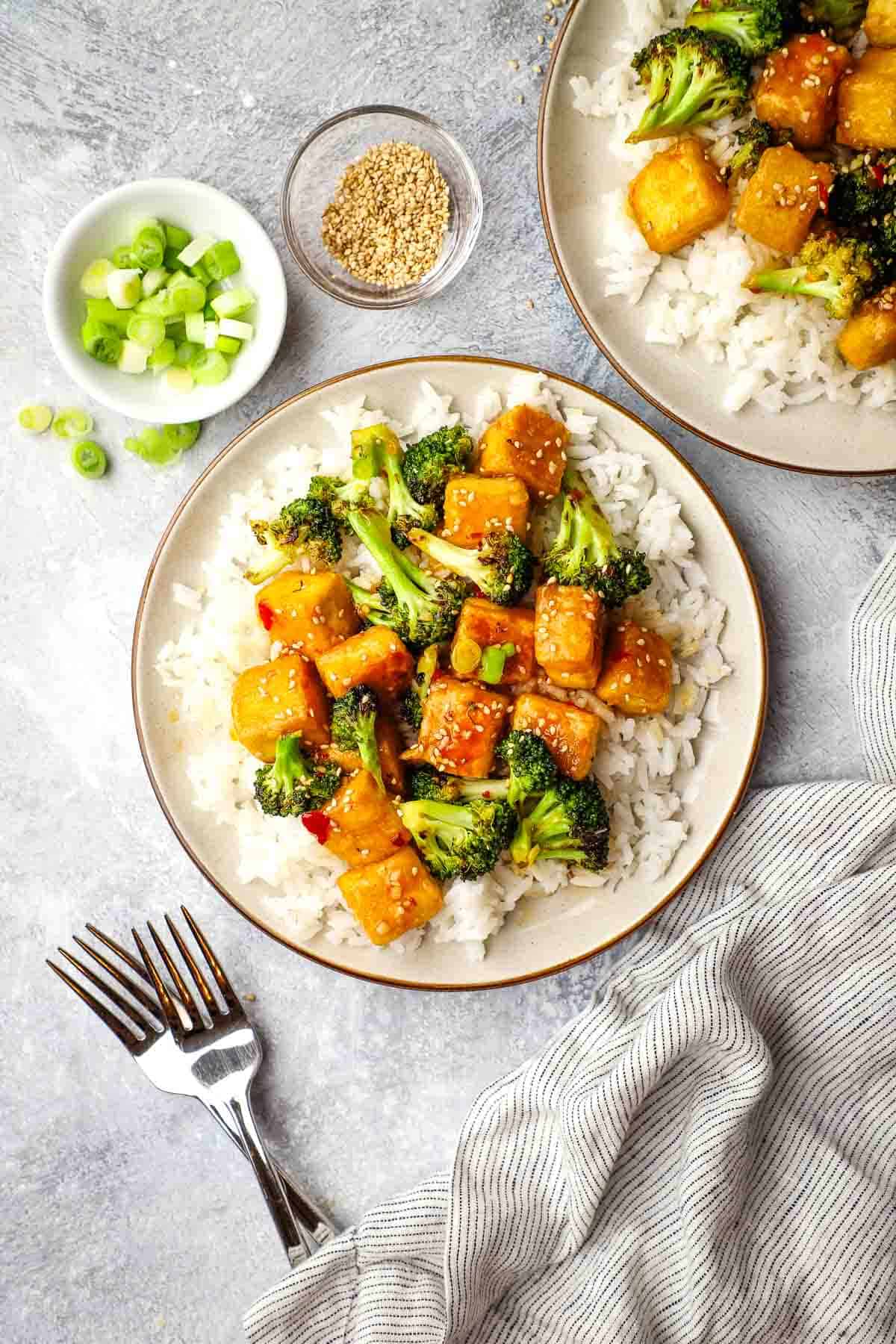 Overhead view of two plates of glazed tofu and broccoli on a bed of white rice.