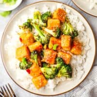 Overhead view of a plate of glazed tofu cubes and broccoli on a bed o white rice.
