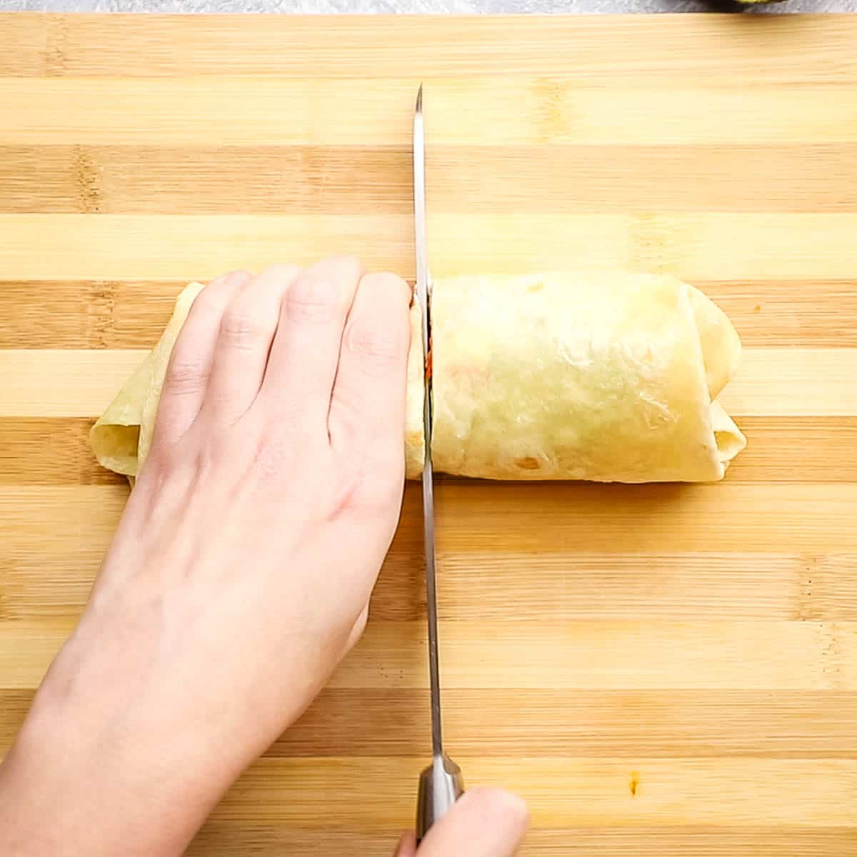 cutting a chicken fajita wrap in half on a cutting board