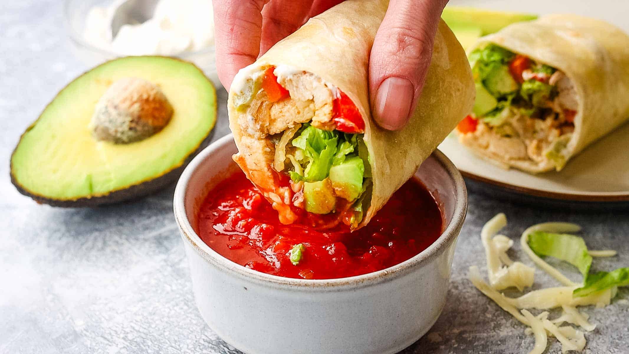 Dipping half-cut chicken fajita wrap in a bowl of salsa.