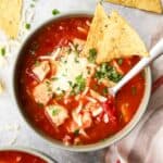 overhead view of a bowl of chipotle chicken soup topped with sour cream, cheese, and tortilla chips