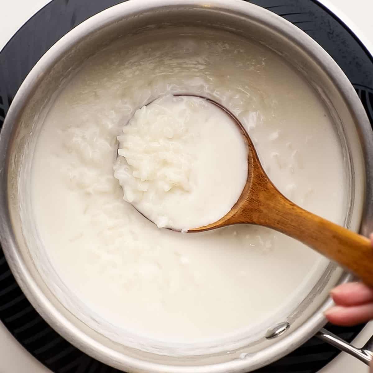 milk mixture and rice simmering in a pot with a wooden spoon in the pot