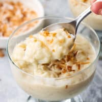 Closeup of a dessert cup of rice pudding garnished with toasted coconut, with a spoon digging in.