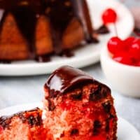 a slice of chocolate cherry cake on a plate with a whole chocolate cherry cake in the background