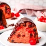 a slice of chocolate cherry cake on a plate with a whole chocolate cherry cake in the background