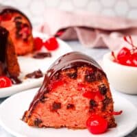 a slice of chocolate cherry cake on a plate with a whole chocolate cherry cake in the background