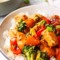 A bowl of chicken teriyaki with vegetables stir fry on a bed of rice with a bowl of rice in the background.