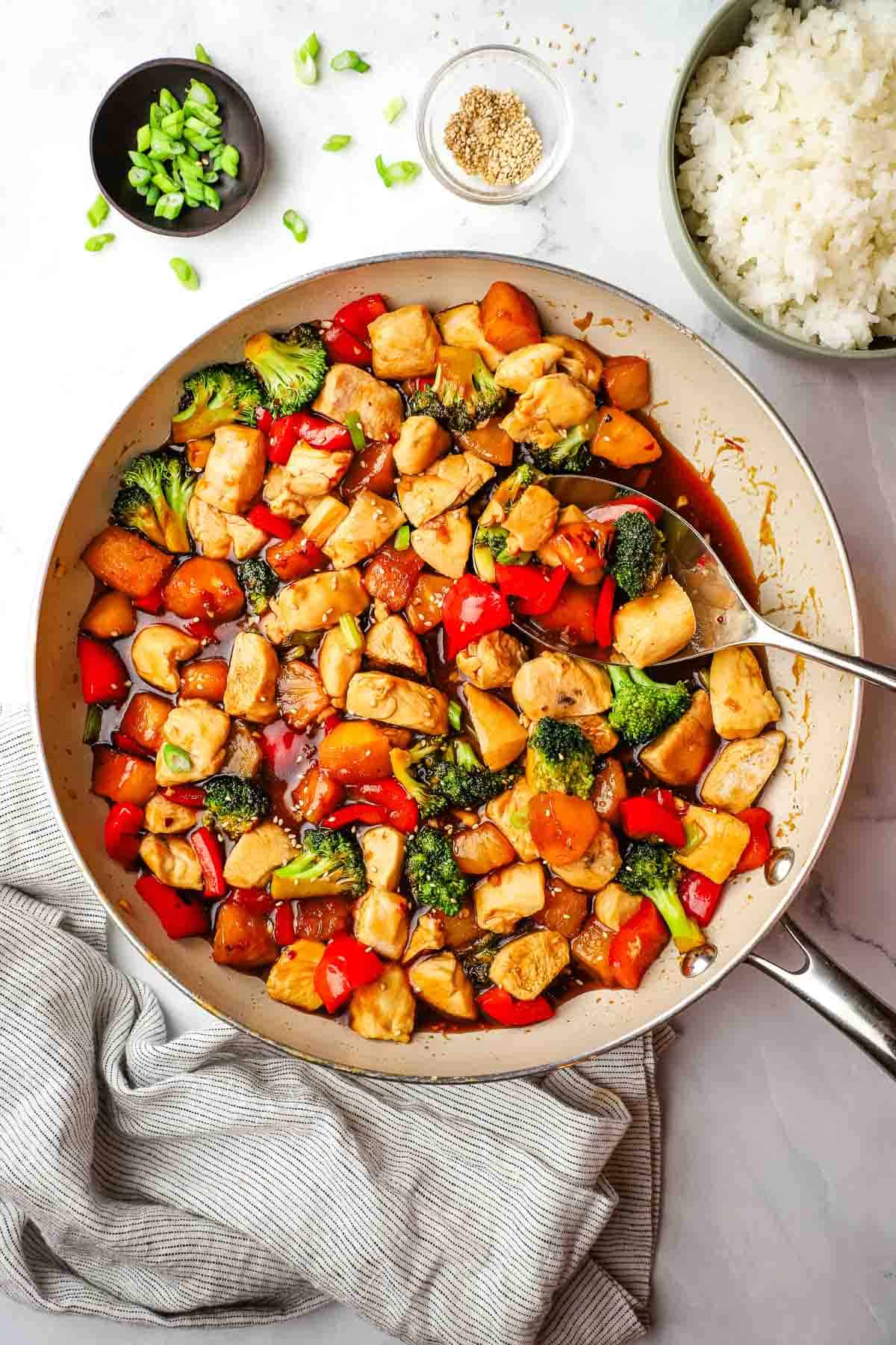 A pan of pineapple chicken teriyaki with vegetables stir fry with a bowl of rice in the background.