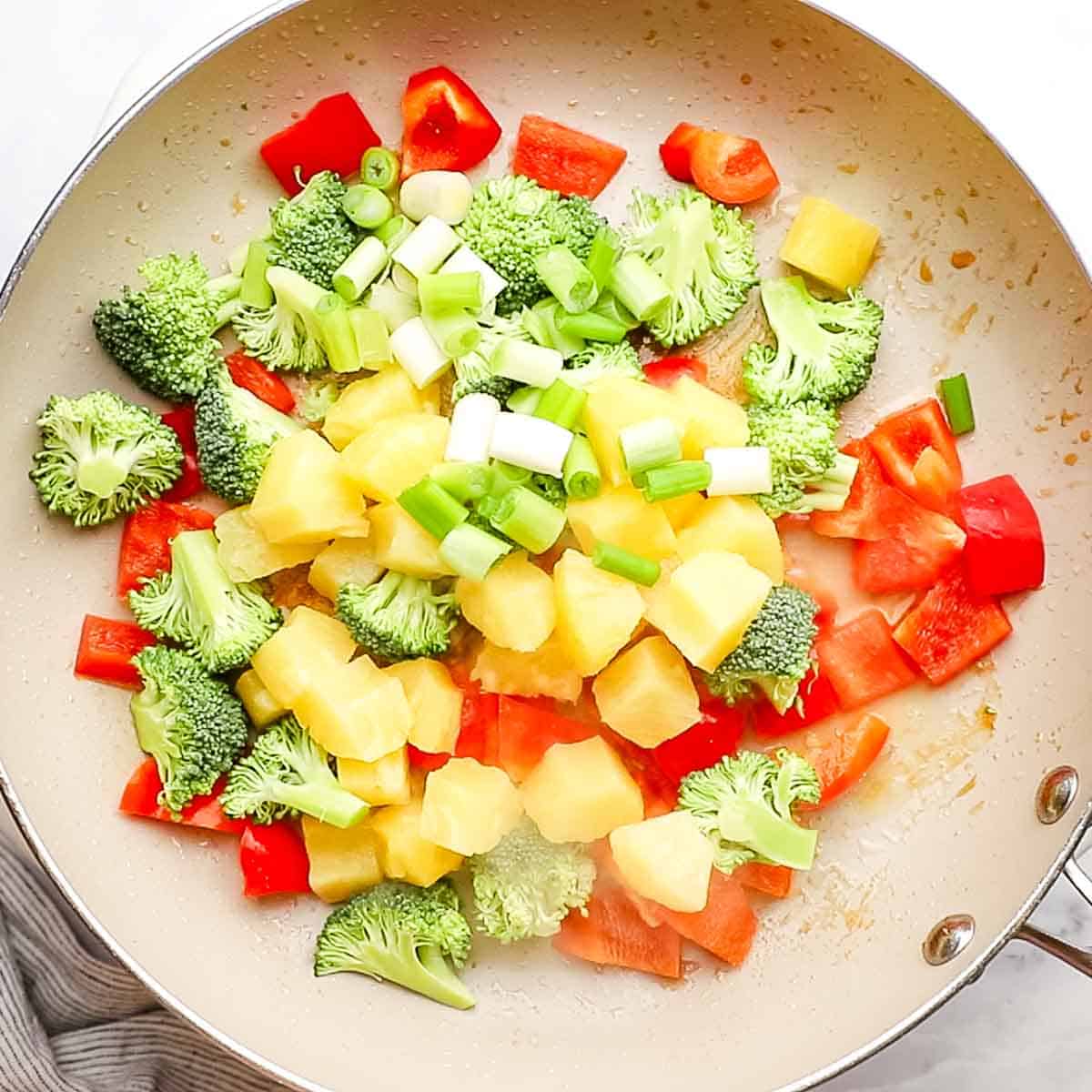 overhead view of vegetables and pineapple being cooked in a large skillet